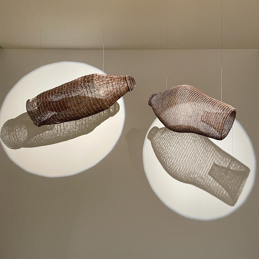 Two fishing baskets hanging at a slight angle, lit from the front casting a shadow on the wall behind that revels their form