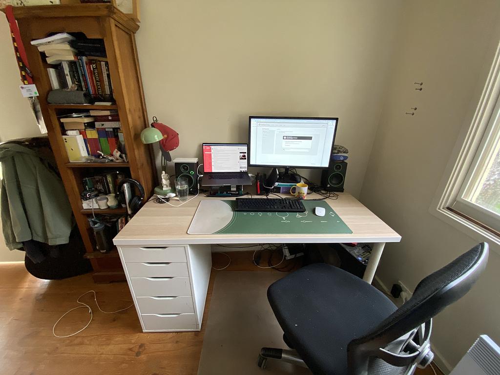 A photo I took of my office for OHS compliance. It shows a desk with a laptop connected to an external monitor side-by-side as well as a book-shelf full of books.